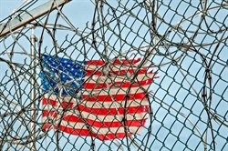 American flag pictured behind barbwire and a chain-link fence