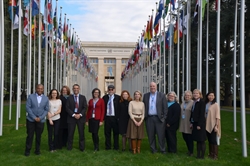 [ai] A diverse group of professionals standing together outside the United Nations building in Geneva, surrounded by flags from various countries. The scene captures a formal gathering with a mix of attire.