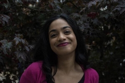 [ai] A woman smiling softly in front of a backdrop of dark leaves, wearing a pink cardigan over a black top.