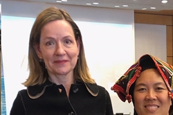 [ai] Two women posing for a photo at an indoor event. One woman, wearing a black coat, appears to be smiling, while the other, in traditional attire with a colorful headpiece, stands beside her. A plain backdrop is visible.