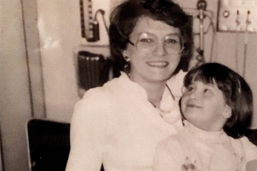 [ai] A black and white photo of a woman and a young girl smiling. The woman, wearing glasses and a white blouse, holds the girl, who looks up at her with a joyful expression.