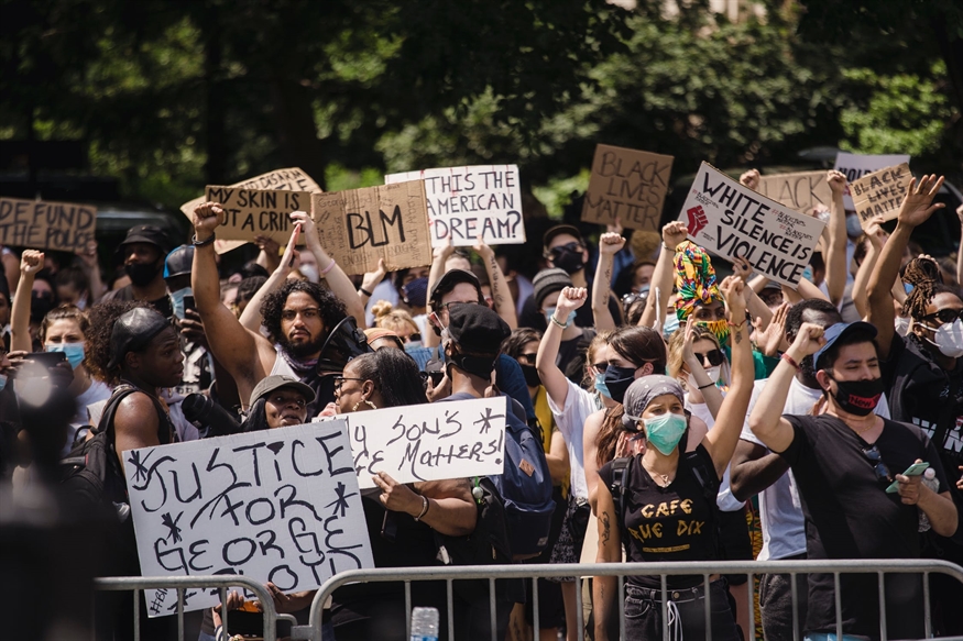 [ai] A diverse crowd of protesters holding signs at a rally, many wearing masks. Signs include messages like "Justice for George Floyd" and "Black Lives Matter," with people raising their fists in solidarity.