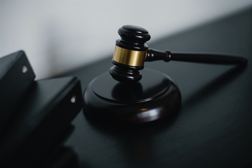[ai] A wooden gavel with a gold band resting on a dark surface next to black binders. The background is softly blurred, focusing on the gavel.